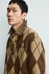 Polo de corte relajado confeccionada en tejido de textura con diseño de rombos en tonos marrones. Presenta cuello de solapa en pana, cierre frontal con botones, mangas largas con puños abotonados y bordado a contraste en el pecho.