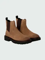 Botas tipo Chelsea Boss modelo Julyo-Cheb, confeccionadas en gamuza color tostado. Presentan paneles laterales elásticos en color marrón oscuro, tirador en el talón y suela de goma dentada de estilo track.