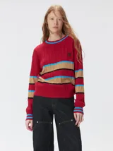 Sweater de punto cable con diseño a rayas horizontales en tonos marrón, amarillo y lila. Presenta cuello redondo acanalado, mangas largas con puños a juego y logo bordado en el pecho.