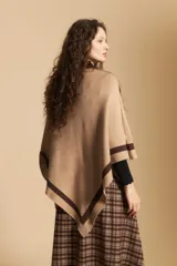 Poncho de silueta amplia y caída fluida, color beige con detalles de líneas en contraste color marrón en los bordes.