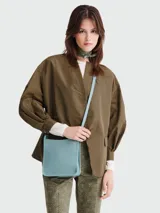 Bandolera pequeña de cuero granulado color celeste claro, con correa ajustable y logo grabado sutilmente en el frente.