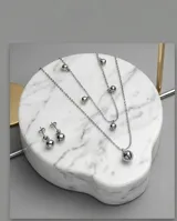 Set de joyería compuesto por un collar de tres cadenas finas con dijes de esferas metálicas y un par de aros colgantes con diseño de esfera. Fabricado en acero italiano.