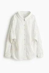 Camisa oversized blanca con finas rayas verticales beige, de manga larga y cierre frontal con botones.