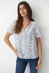 Blusa blanca con estampado floral celeste, escote en V y mangas cortas.