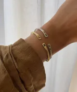Pulsera rígida abierta en color dorado, con iniciales grabadas en los extremos.