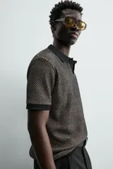 Polo de manga corta con cuello solapa y cierre frontal de dos botones. Tejido de punto con textura de rombos en tonos negro y beige, con ribetes negros en cuello, mangas y bajo.