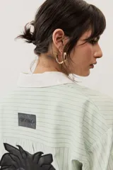 Camisa oversize a rayas color verde menta con cuello y puños en contraste de color blanco. Presenta cierre frontal con botones y un bolsillo aplicado en el pecho.