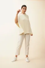 Poncho color crema de tejido de punto industrial con cuello alto y aberturas laterales para los brazos.