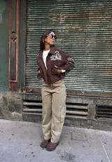 Campera tipo bomber color chocolate, confeccionada en gamuza, con cierre frontal y bordados en color natural con diseño de arabescos en el pecho y las mangas.