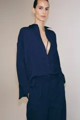 Camisa de corte oversize confeccionada en mezcla de viscosa con textura de rayas verticales en jacquard. Presenta cuello solapa, cierre frontal con botones, bolsillo de plastrón en el pecho, mangas largas con puños anchos y bajo redondeado.