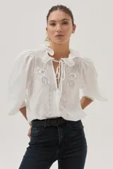 Blusa blanca con lunares en relieve, cuello con volados y lazos, mangas abullonadas 3/4 y bordados con lentejuelas en el frente.