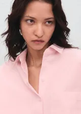 Camisa de corte oversize en color rosa claro, con cuello camisero, cierre frontal de botones, manga larga con puños abotonados y un bolsillo de parche en el pecho.