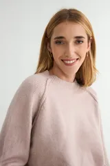 Buzo de tejido de punto en color rosado, con cuello redondo, mangas largas y puños acanalados. Presenta un diseño de tejido texturizado en la parte inferior y en los puños.