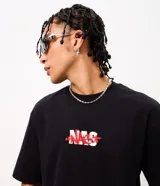 Remera negra de algodón con cuello redondo, manga corta y calce relaxed. Presenta una gran estampa en la espalda con la palabra "NAS" en rojo, la imagen del rapero y gráficos alegóricos de Nueva York.