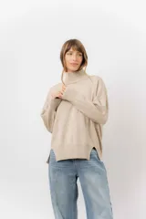 Sweater de tejido de punto color beige, con cuello alto, hombros caídos, mangas largas con puños acanalados y tajos laterales en el ruedo.