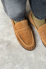 Mocasín de gamuza color tostado, con diseño clásico de antifaz en el empeine y costuras artesanales fruncidas alrededor de la puntera.