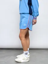 Short de felpa celeste, de corte deportivo, con detalles de pipings tricolor en los bordes y escudo del Club Nacional de Football aplicado en la pierna.
