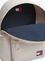 Mochila Tommy Jeans de color beige, diseño compacto y curvo, con compartimento principal con cierre de cremallera, bolsillo frontal con cremallera y parche con el logo de la marca. Cuenta con asas ajustables y acolchadas.