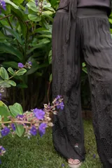 Conjunto de dos piezas color negro, compuesto por un pantalón ancho de tiro alto con detalle de encaje en el ruedo y una blusa holgada de manga larga con escote drapeado y nudo frontal.