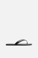 Sandalia minimalista de cuero negro, con tira delgada en el empeine y suela plana.