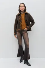 Chaqueta de lana merino hervida color marrón, con cuello camisero y botones forrados. Presenta bordados artesanales en color ocre que recorren el frente, el cuello y los puños.