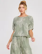 Blusa corta de lino y viscosa color beige, con bordado de grandes flores al tono, cuello redondo, mangas cortas abullonadas y corte holgado.