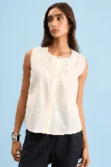 Blusa sin mangas de algodón color crudo, con cuello redondo, corte relajado y detalles de costuras y pespuntes en contraste.