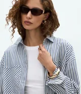 Camisa de jean de manga larga con diseño de rayas verticales, cuello inglés, cierre frontal con botones y dos bolsillos grandes en el frente.