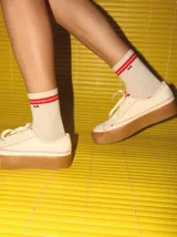 Championes bajos color crema con pespuntes rojos, capellada de tela canvas y plataforma de goma color caramelo de 4 cm de altura.