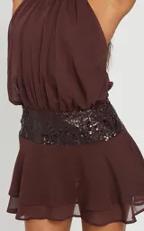 Vestido corto color marrón, con cuello halter, falda con volados y una faja central decorada con lentejuelas brillantes.