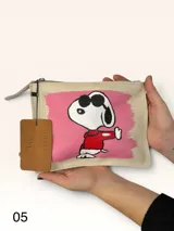 Sobre de cuero marrón con diseño pintado a mano que presenta al personaje Snoopy sobre un fondo rosado y la palabra 'heal'. Cuenta con cierre superior y etiqueta de cuero colgante.