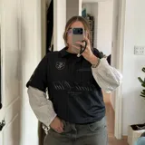 Camiseta de fútbol estilo boxy de manga corta y cuello polo, en color negro con sutiles rayas verticales. Presenta inscripciones estampadas y escudo bordado en el pecho.