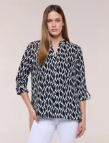 Blusa de calce suelto y caída ligera en color negro con estampado geométrico blanco. Presenta escote en V, cuello mao, abotonadura frontal metálica y bolsillos superiores en el pecho. Cuenta con mangas largas regulables con presilla y botón, ruedo redondeado con tajos laterales y canesú en la espalda.