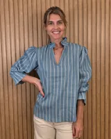 Blusa de algodón a rayas celestes y blancas, con cuello alto con volados, escote en V y mangas abullonadas tres cuartos.