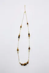 Collar largo dorado con cadena fina eslabonada y cuentas cilíndricas de piedra ojo de tigre a lo largo de su diseño.