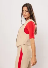 Chaleco beige con escote en V, sin mangas y cierre frontal con botones. Presenta pespuntes en color rojo y logo bordado en la espalda.