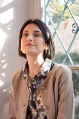 Cardigan de punto color beige con cuello redondo, cierre frontal con botones dorados, bolsillos frontales y terminaciones en crochet. Presenta hombreras internas y diseño de corte recto.