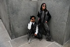 Mono de denim con efecto de lavado ácido en tonos grisáceos y negros. Presenta cierre frontal completo, cuello alto, bolsillos laterales y bordados decorativos en color azul en la parte superior del pecho. De diseño utilitario y corte holgado.