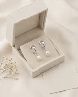 Caravanas colgantes de plata 925, compuestas por un aro pequeño con incrustaciones de circonia y una perla natural en forma de gota.