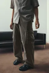 Pantalón cargo de sarga de algodón suave con efecto lavado, color marrón verdoso. Presenta cintura elástica con cordón ajustable, bolsillos laterales, bolsillos cargo con solapa en las piernas y cordón ajustable en el bajo. Corte holgado.