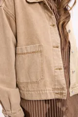 Campera de denim en tono beige, de corte cropped, con cuello camisero, cierre frontal con botones metálicos y bolsillos frontales tipo parche.
