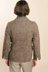 Chaqueta marrón de lana con cuello, solapa y bolsillos ojal. Forro solo en las mangas y terminaciones envivadas. Esquinas redondeadas y mangas con corte en puño que permiten transformarla en manga 3/4. Más larga en la espalda que en la delantera. Abrochadura con dos botones.