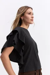 Remera negra de algodón con mangas cortas que presentan volados dobles, aportando volumen y movimiento a la prenda.