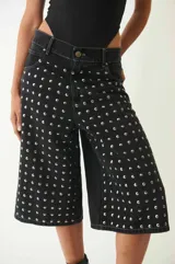 Bermuda de denim negro con tachas redondas plateadas, tiro bajo, cuatro bolsillos, pasacintos y cierre con botón metálico.