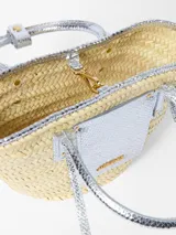 Canasto tejido a mano en fibra vegetal de Jacquemus, modelo Le Petit Panier Soli, con detalles, asas cortas y bolsillo frontal de cuero con acabado metalizado plateado, y logo grabado en letras doradas.