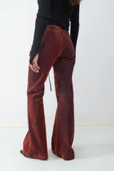 Pantalón de denim con acabado flocked que le otorga una textura aterciopelada, de tiro medio y corte flare. Presenta un cierre frontal con cordones y ojales metálicos, costuras verticales decorativas y paneles laterales en contraste.