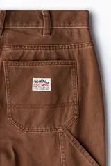 Pantalón worker marrón de sarga de algodón gruesa, con piernas rectas y corte relaxed fit. Presenta cintura clásica con cierre de botón, bolsillos al bies, bolsillo monedero, bolsillos traseros, trabilla funcional en un lateral y bolsillo cargo dividido en dos en el otro.