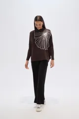Sweater de tejido marrón oscuro con cuello alto y un gran aplique bordado en blanco con diseño abstracto que simula un abanico o flor.