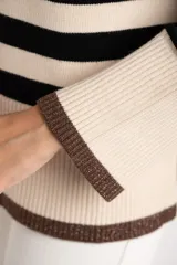 Sweater de punto a rayas horizontales negras y crudas, con cuello redondo y mangas largas. Tiene ribete marrón en puños y ruedo.