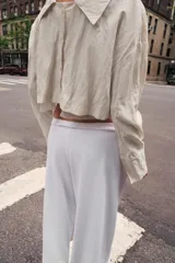 Camisa corta de manga larga con cuello solapa y cierre frontal de botones. Presenta un tejido con efecto arrugado y un diseño con forro interior semitransparente que sobresale en el ruedo.